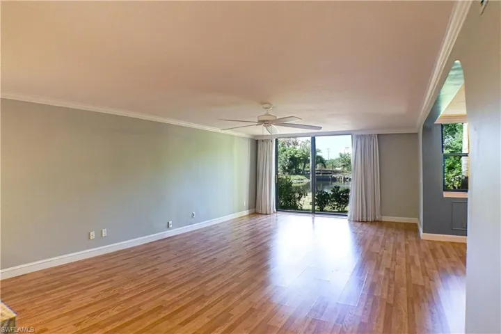 Unfurnished room with a ceiling fan, crown molding, light wood finished floors, and expansive windows