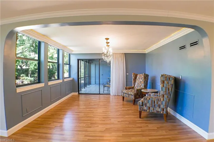 Sitting room with arched walkways, light wood-style floors, suspended lighting, and ornamental molding