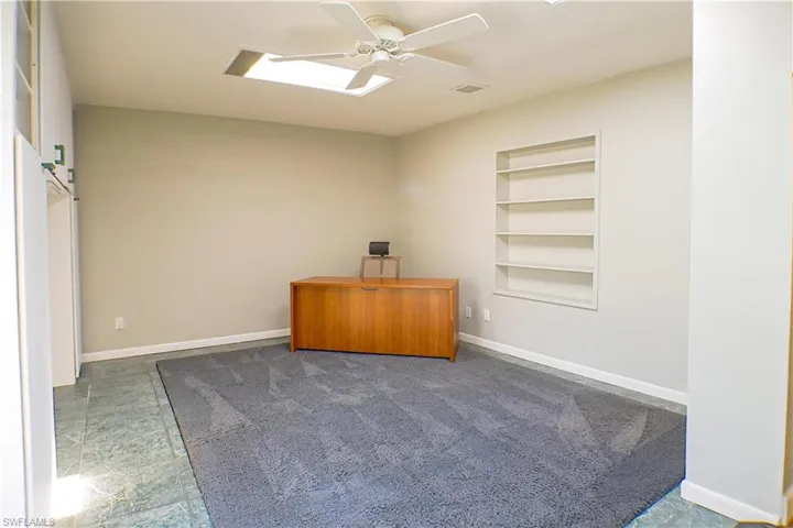 Carpeted spare room featuring built in features, ceiling fan, and a desk
