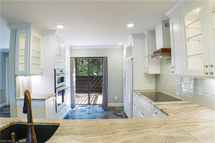 Kitchen with glass fronted cabinets, white cabinets, freestanding refrigerator, dark stone finish floors, and black electric cooktop