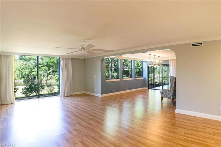 Spare room featuring arched walkways, ceiling fan, light wood-type flooring, suspended lighting, and crown molding