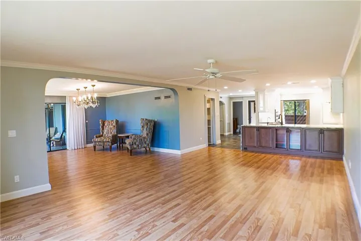 Unfurnished living room with arched walkways, light wood finished floors, ornamental molding, ceiling fan, and a chandelier