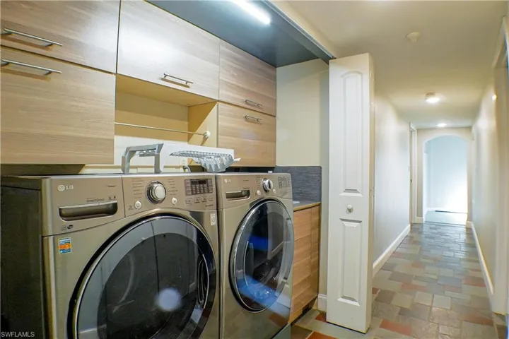 Laundry area with separate washer and dryer, arched walkways, and light stone finish flooring
