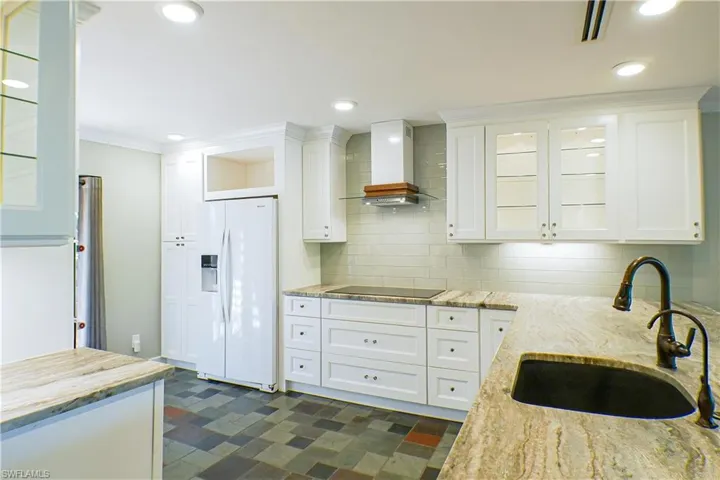 Kitchen featuring white refrigerator with ice dispenser, white cabinetry, light stone counters, glass insert cabinets, and ornamental molding