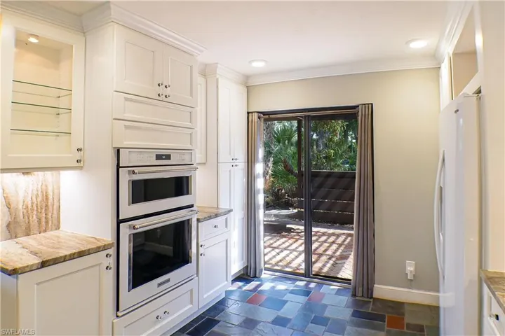 Kitchen featuring white appliances, white cabinetry, crown molding, dark stone finish flooring, and recessed lighting
