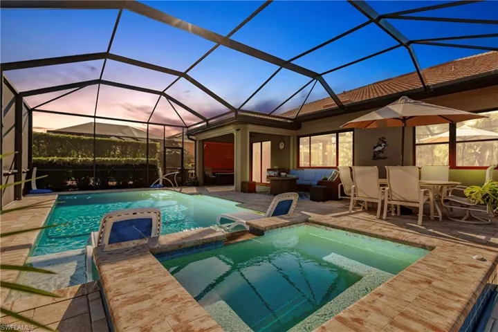 Pool at dusk with an in ground hot tub, outdoor lounge area and lanai