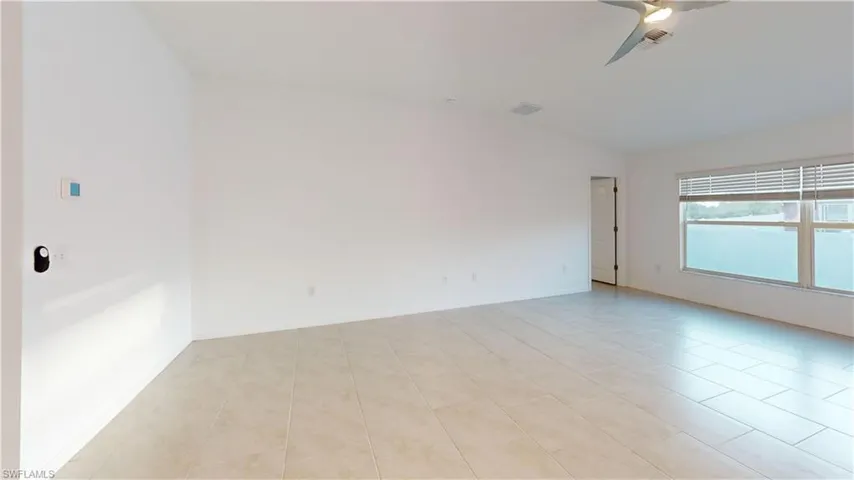 Spacious interior room featuring light-toned tile flooring, large windows with horizontal blinds, a modern ceiling fan with integrated lighting, and neutral wall finishes