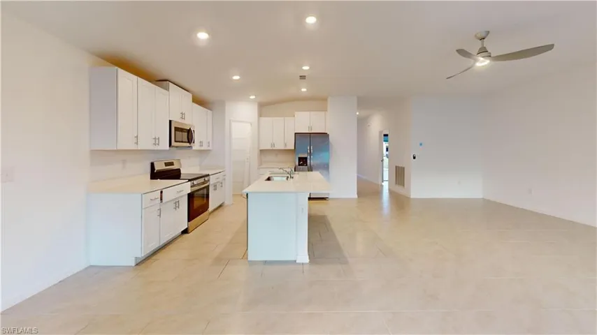 Open-concept living area featuring a kitchen island with sink, stainless steel appliances, white cabinetry, recessed lighting, and a ceiling fan