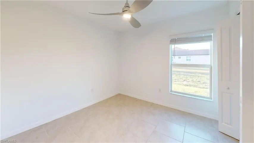 Spacious room featuring neutral-toned tile flooring, a large window with horizontal blinds, and a contemporary ceiling fan