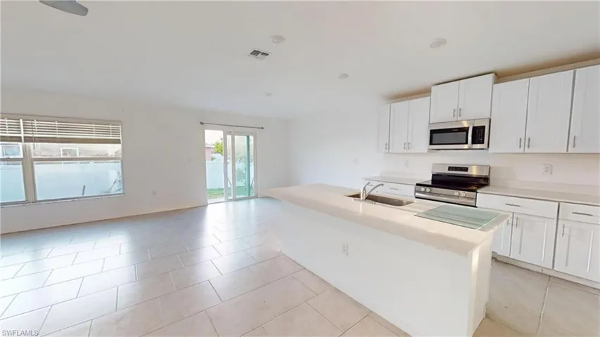 Open-concept living space featuring a kitchen island with sink, stainless steel appliances, white cabinetry, tile flooring, and sliding glass doors to the exterior