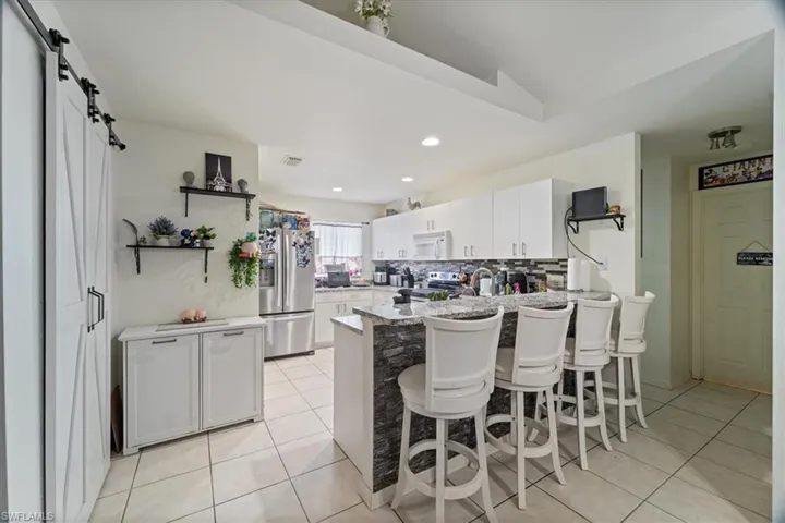 Kitchen with a barn door, white cabinetry, a kitchen bar, stainless steel appliances, and tasteful backsplash