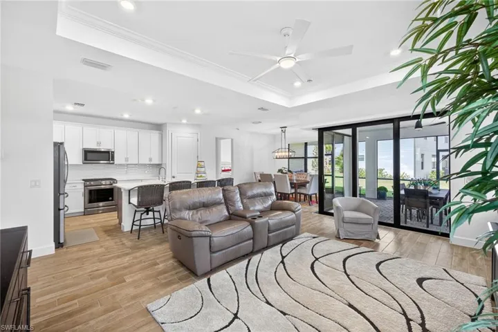 Living room with crown molding, a raised ceiling, light wood-style floors, ceiling fan, and recessed lighting