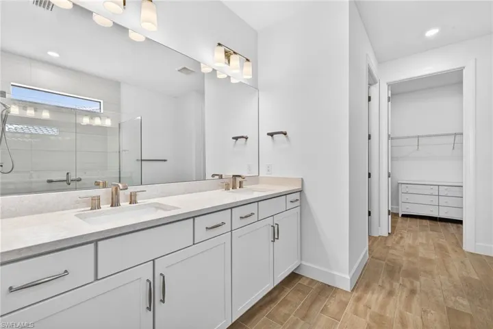Full bathroom featuring a stall shower, double vanity, a walk in closet, light wood-style flooring, and recessed lighting