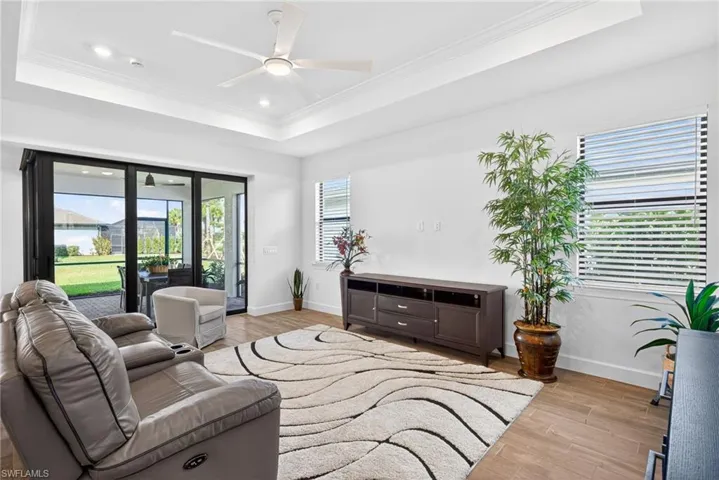 Living room featuring a raised ceiling, ceiling fan, light wood-type flooring, crown molding, and recessed lighting