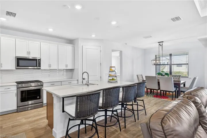 Kitchen with stainless steel appliances, light wood-style flooring, tasteful backsplash, and white cabinetry