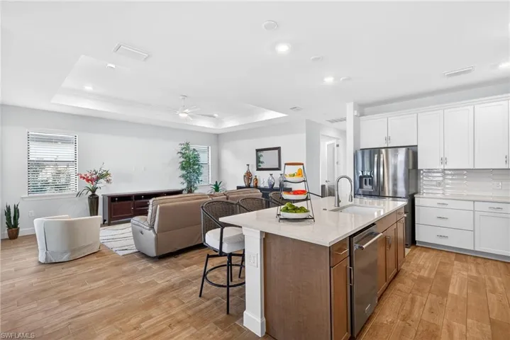 Two tone kitchen with open floor plan, light stone countertops, two tone cabinets, light wood-style flooring, and a ceiling fan