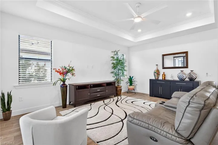 Living room with ceiling fan, light wood-type flooring, crown molding, a tray ceiling, and recessed lighting