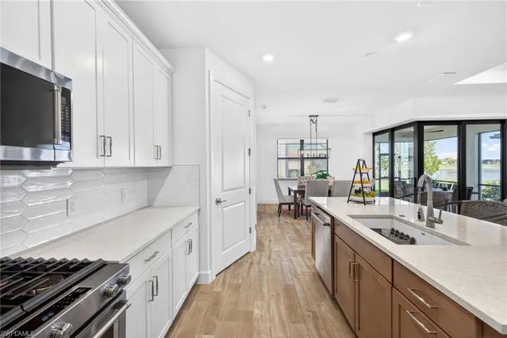 Dual tone kitchen featuring stainless steel appliances, two tone color scheme, light stone countertops, light wood-type flooring, and decorative backsplash