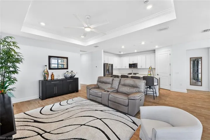 Living area featuring ceiling fan, light wood-type flooring, crown molding, a tray ceiling, and recessed lighting