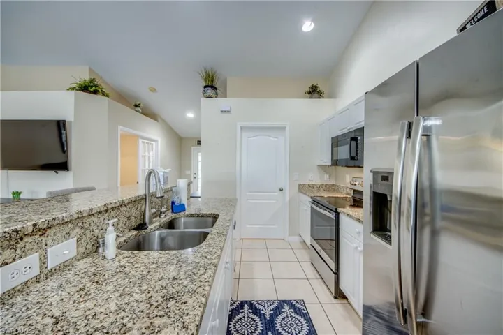 Kitchen featuring white cabinetry, sink, light stone counters, vaulted ceiling, and appliances with stainless steel finishes