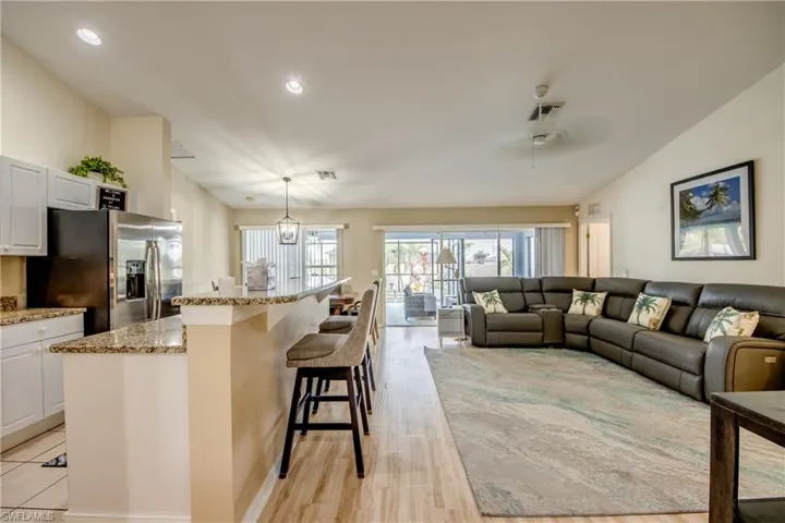 Kitchen with stainless steel refrigerator with ice dispenser, pendant lighting, white cabinetry, light hardwood / wood-style flooring, and a kitchen island