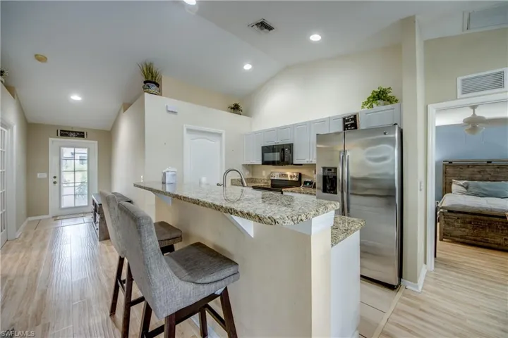 Kitchen featuring light stone countertops, light hardwood / wood-style floors, a kitchen bar, white cabinetry, and stainless steel appliances