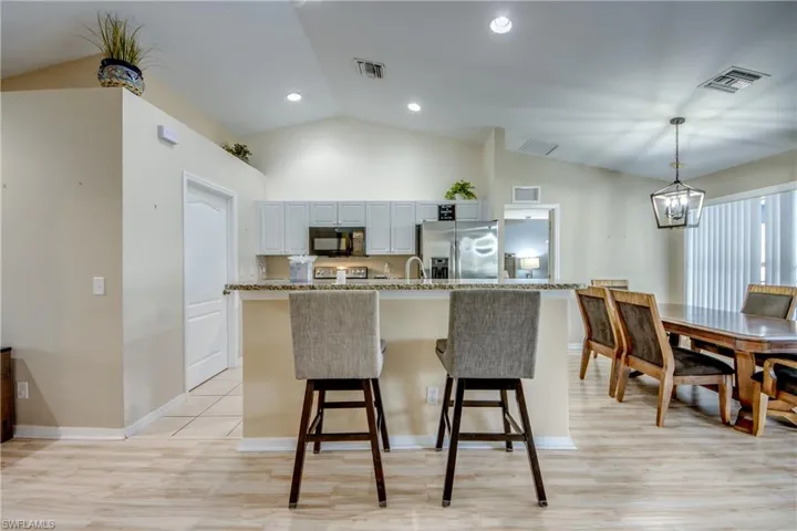 Kitchen featuring stainless steel refrigerator with ice dispenser, hanging light fixtures, vaulted ceiling, light wood-type flooring, and light stone counters