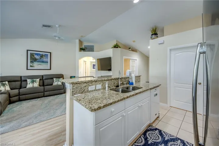 Kitchen with vaulted ceiling, a center island with sink, white cabinetry, and sink