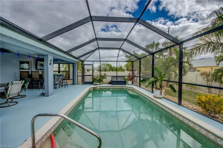 View of pool featuring exterior bar, glass enclosure, and a patio area