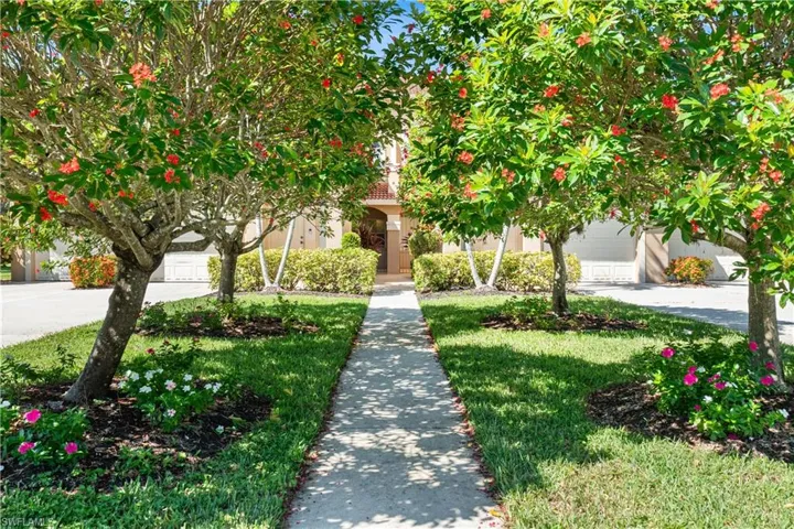 View of property hidden behind natural elements with concrete driveway, a front yard, and stucco siding