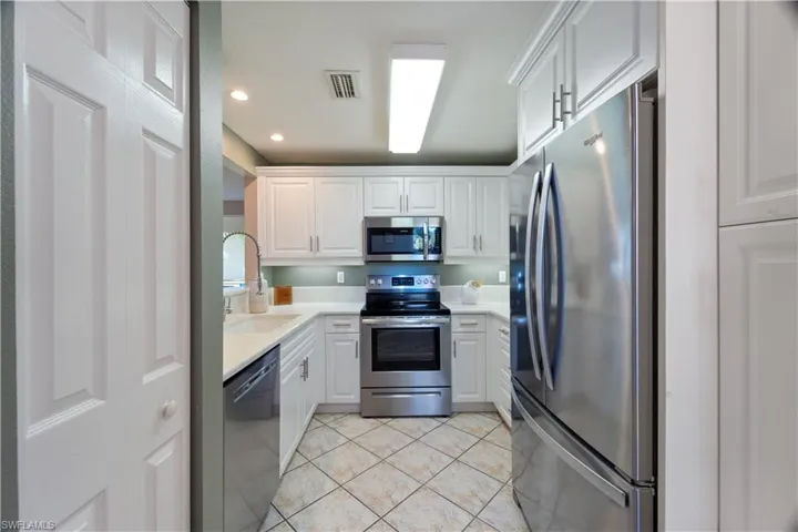 Kitchen with white cabinetry, stainless steel appliances, light tile patterned floors, recessed lighting, and light stone counters