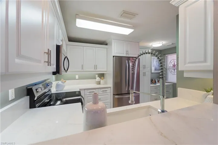 Kitchen featuring stainless steel appliances, light stone countertops, and white cabinets