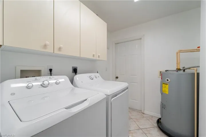 Laundry room featuring electric water heater, light tile patterned floors, cabinet space, and washing machine and dryer