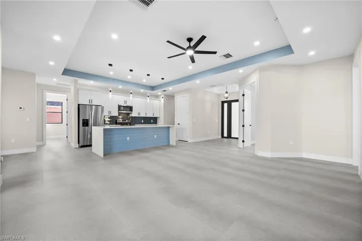 Unfurnished living room featuring ceiling fan, sink, and a tray ceiling