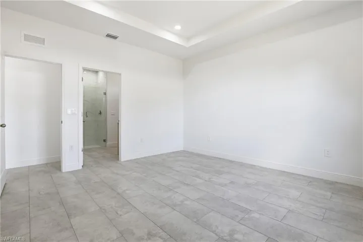 Unfurnished bedroom featuring ensuite bathroom, a raised ceiling, and recessed lighting