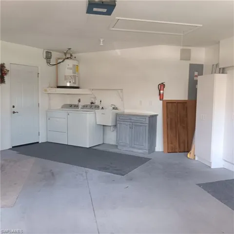 Garage with sink, washer and clothes dryer, electric water heater, and a garage door opener