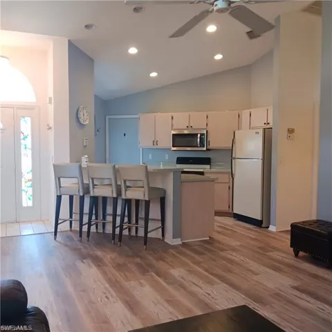 Kitchen with a kitchen bar, wood-type flooring, white appliances, ceiling fan, and kitchen peninsula
