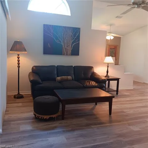 Living room with ceiling fan, high vaulted ceiling, and wood-type flooring