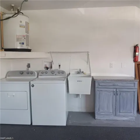 Clothes washing area featuring sink, independent washer and dryer, water heater, and cabinets