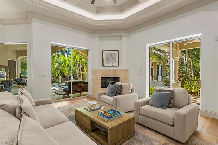 Living room with a ceiling fan, wood-type flooring, a premium fireplace, crown molding, and a high ceiling