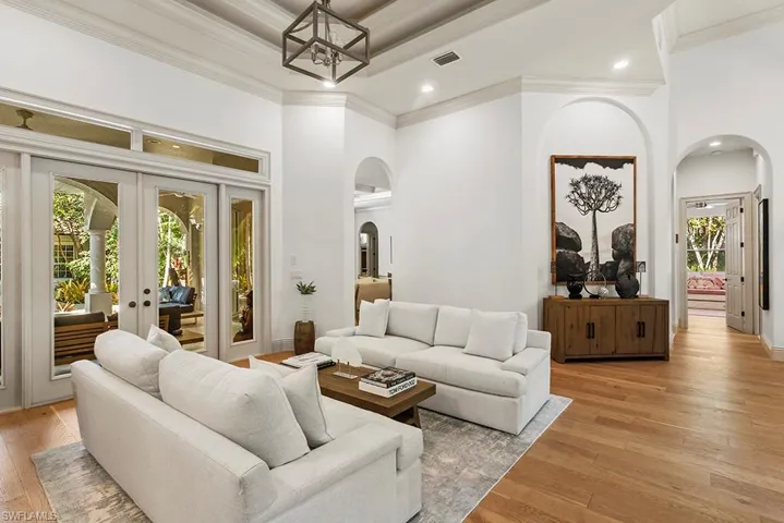 Living area featuring arched walkways, light wood-style floors, french doors, a high ceiling, and recessed lighting