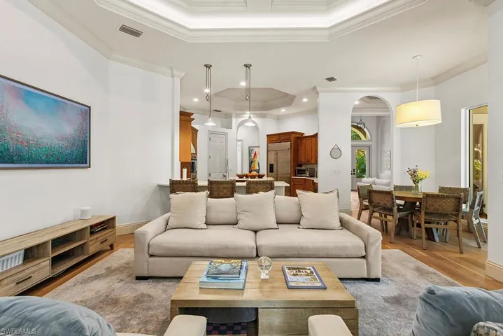 Living area featuring a tray ceiling, arched walkways, light wood-style flooring, ornamental molding, and recessed lighting