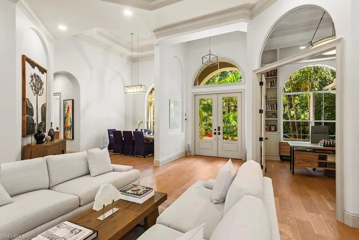 Living area featuring a desk, light wood-style floors, french doors, arched walkways, and a high ceiling