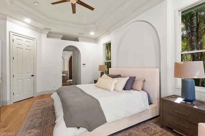 Bedroom with a raised ceiling, ceiling fan, wood finished floors, arched walkways, and ornamental molding