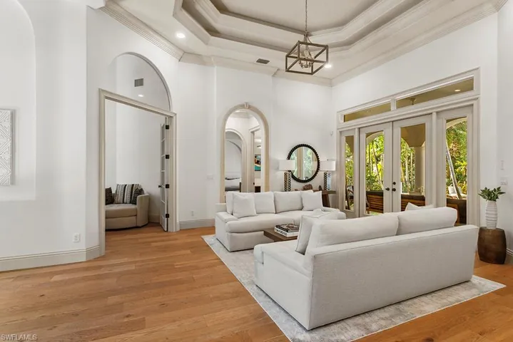 Living area featuring a high tray ceiling, arched walkways, wood-type flooring, french doors, and ornamental molding