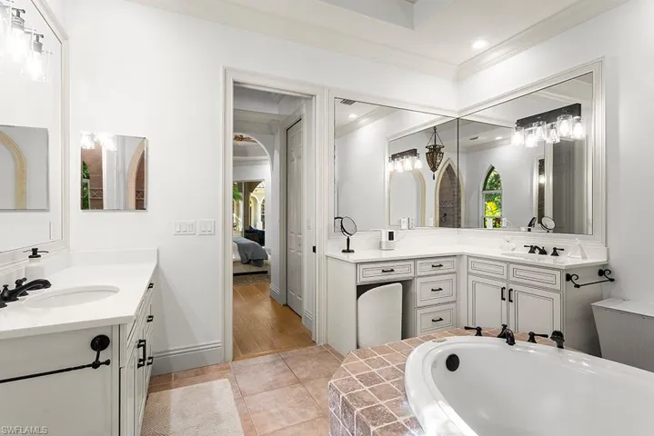 Full bath featuring two vanities, connected bathroom, a bath, ornamental molding, and light tile patterned floors