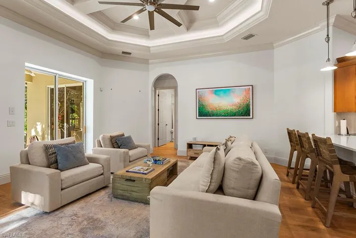 Living room featuring arched walkways, ceiling fan, wood finished floors, coffered ceiling, and crown molding