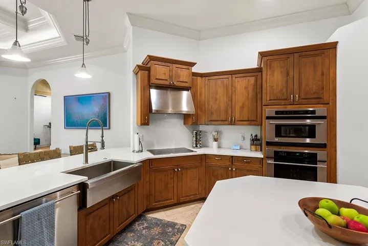 Kitchen featuring stainless steel appliances, decorative light fixtures, ornamental molding, light stone counters, and arched walkways