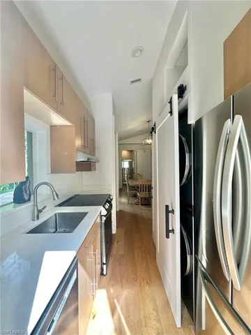 Kitchen featuring stainless steel appliances, light wood finished floors, vaulted ceiling, light stone counters, and modern cabinets