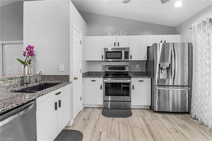 Kitchen featuring ceiling fan, stainless steel appliances, dark stone countertops, sink, and lofted ceiling